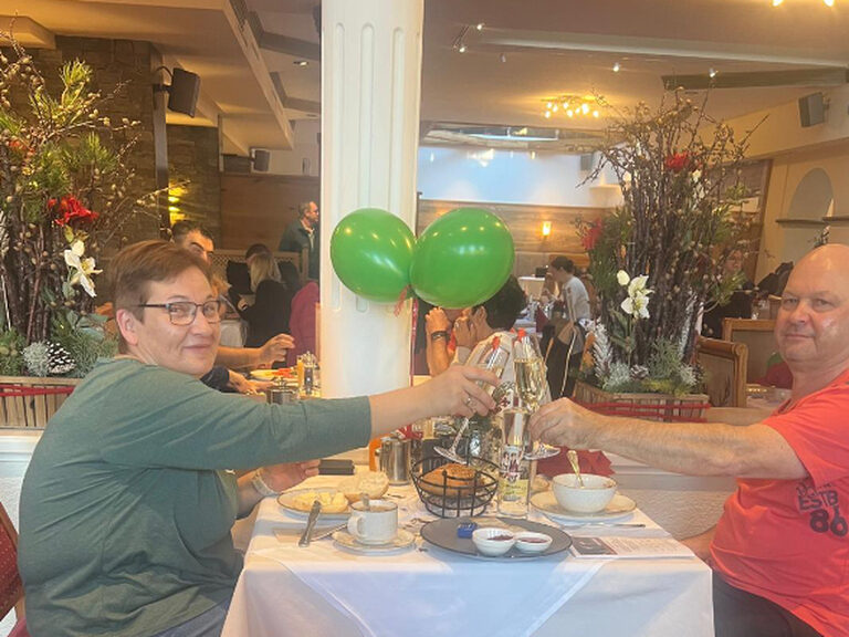 Paar sitzt am dekorierten Frühstückstisch und stößt mit einem Glas Sekt anlässlich Geburtstag an