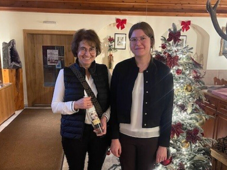 zwei Frauen stehen vor dem beschmückten Weihnachtsbaum und eine der beiden Frauen hält das Geburtstagsgeschenk vom Hotel in der Hand