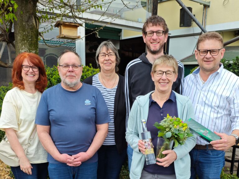 Familie steht vor dem Kohlerhof und das Geburtstagskind hält lächlend einen Blumenstrauß und eine Flasche Schnaps in der Hand