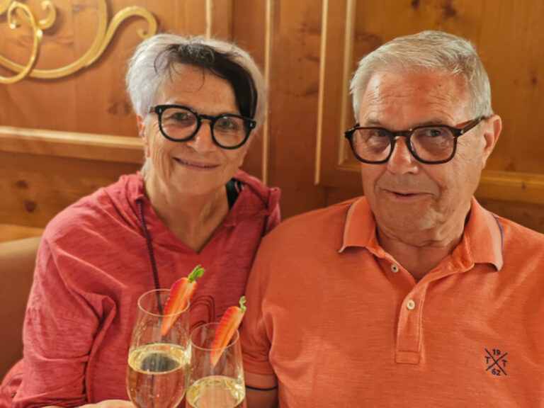 Paar sitzt am Tisch und stößt mit einem Glas Sekt auf den Geburtstag an