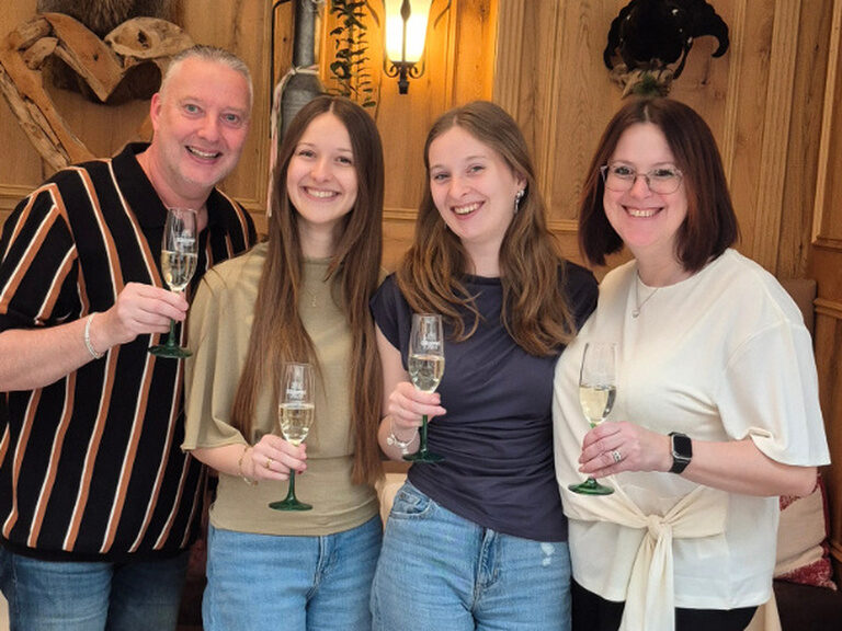 Familie bestehend aus vier Personen stößt mit je einem Glas Sekt lachend anlässlich eines Geburtstags an