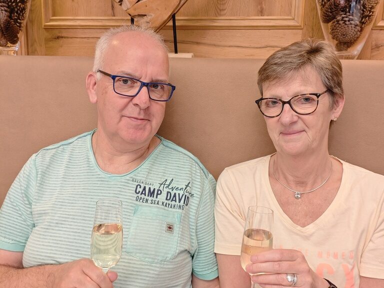 Paar sitzt mit Sektglas am Tisch und posiert anlässlich Geburtstag