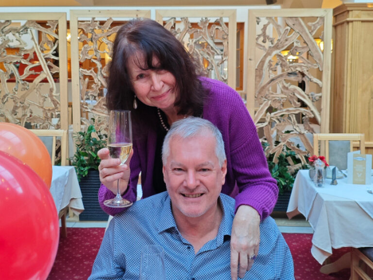 Paar lächelt anlässlich eines Geburtstags mit jeweils einem Glas Sekt in der Hand in die Kamera