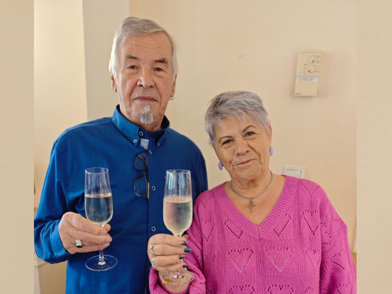 Paar lächelt mit jeweils einem Glas Sekt in der Hand in die Kamera
