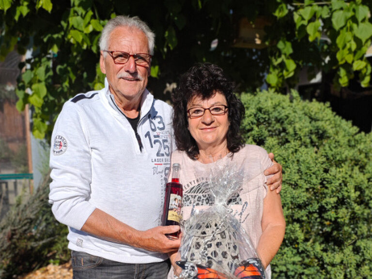 Paar posiert anlässlich Geburtstag mit einem Glas Sekt und Geschenk im Gastgarten des Kohlerhofs