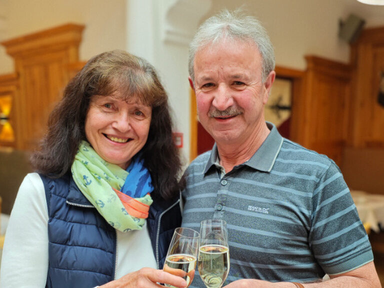 Paar posiert lächelnd mit je einem Glas Sekt in der Hand anlässlich des Geburtstags der Frau