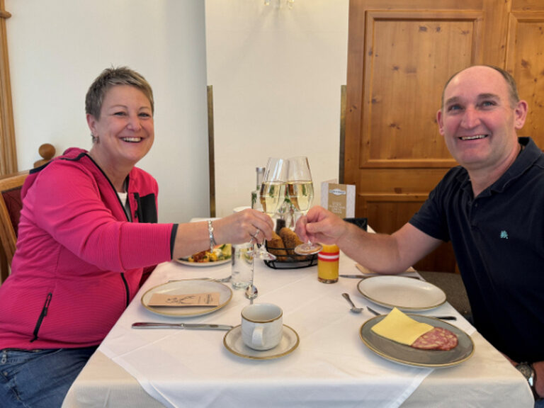 Paar sitzt am gedeckten Frühstückstisch und stößt mit einem Glas Sekt anlässlich eines Geburtstags an.