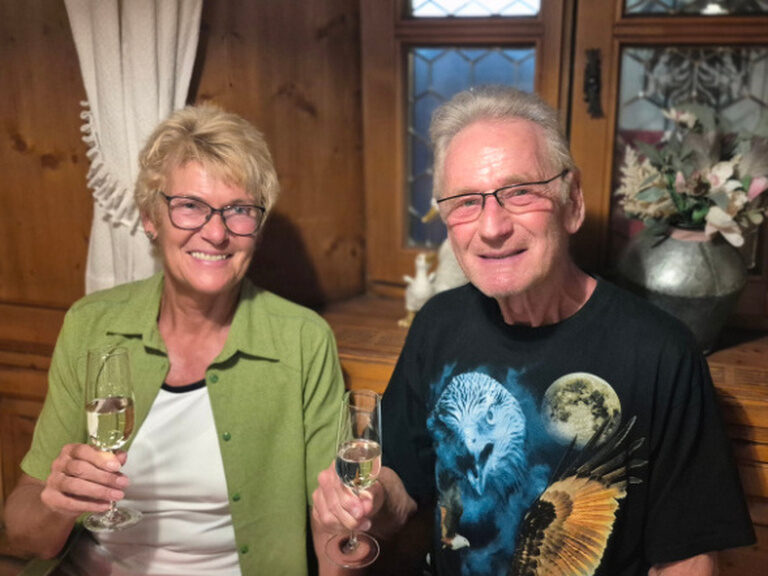 Paar sitzt am Tisch und hält je ein Glas Prosecco in der Hand