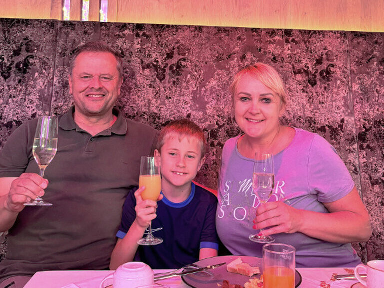 Familie sitzt am Frühstückstisch und stößt mit einem Orangensaft auf einen Geburtstag an
