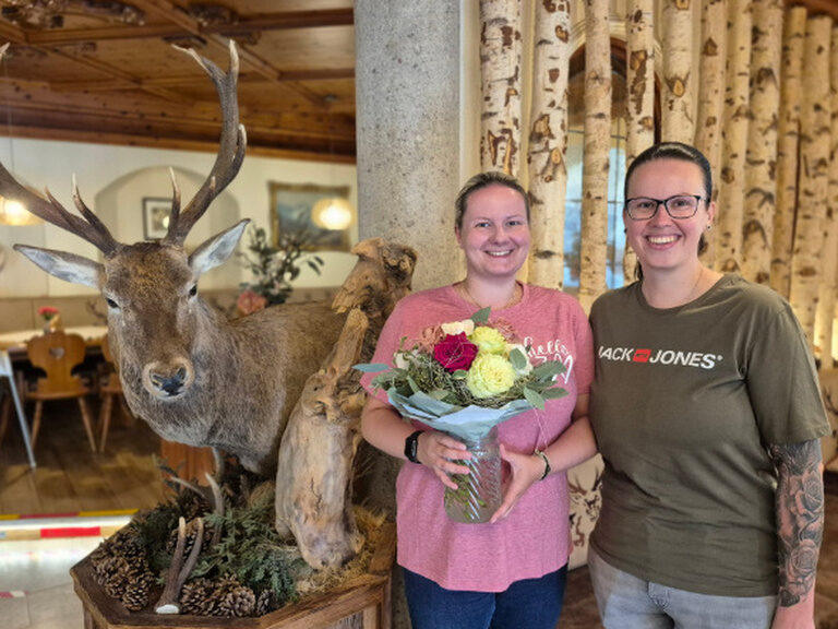 zwei Frauen posieren lächelnd anlässlich eines Geburtstags mit Blumenstrauß in der Hotellobby