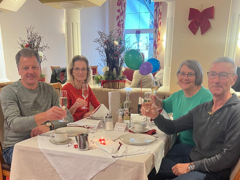 Familie sitzt am dekorierten Frühstückstisch und stößt mit einem Glas Sekt anlässlich eines Geburtstags an