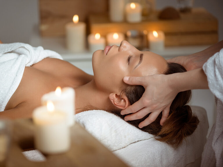 Frau liegt auf einer Massageliege und wird am Kopf massiert