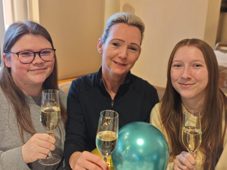 Drei Frauen sitzen am festlich dekorierten Tisch und stoßen mit einem Glas Sekt auf einen Geburtstag an