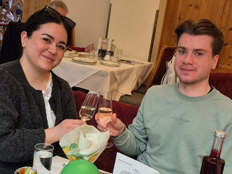 Paar sitzt am dekorierten Frühstückstisch und stößt mit einem Glas Sekt anlässlich eines Geburtstags an