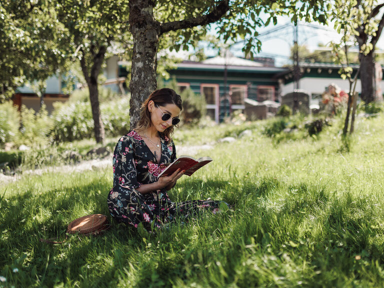 Frau mit Buch in der Hand, unter einem Baum, im Rasen des Romantikparks des Kohlerhofs sitzend