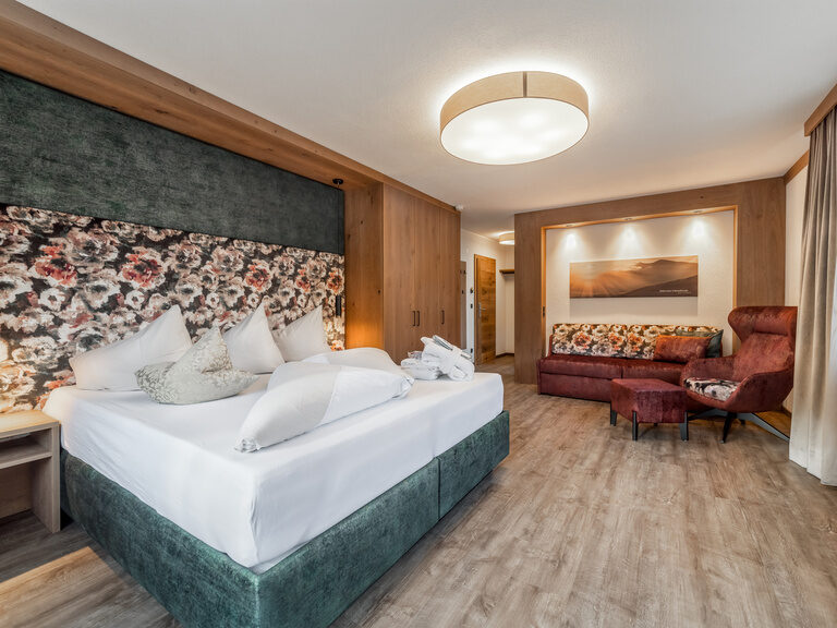 Kuschelsuite in Braun- und Grüntönen, Holzboden, Boxspringbett, Couch, Ohrensessel und Fußhocker