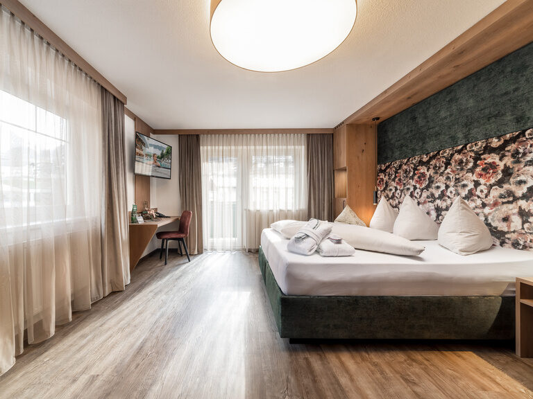 Kuschelsuite in Braun- und Grüntönen, Holzboden, Boxspringbett, Couch, Ohrensessel und Fußhocker