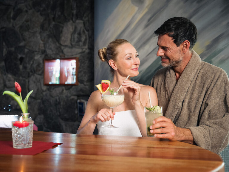 Paar sitzt im Bademantel an der Saunabar und genießt einen Cocktail