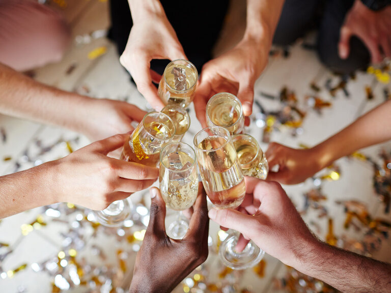 eine Gruppe stoßt mit Sektgläsern an, wobei man nur die Hände und die Gläser sieht