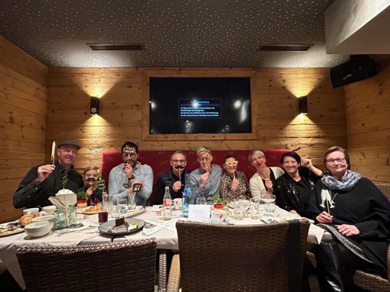 Mehrere Personen sitzen am Frühstückstisch und posieren mit lustigen Pappmasken