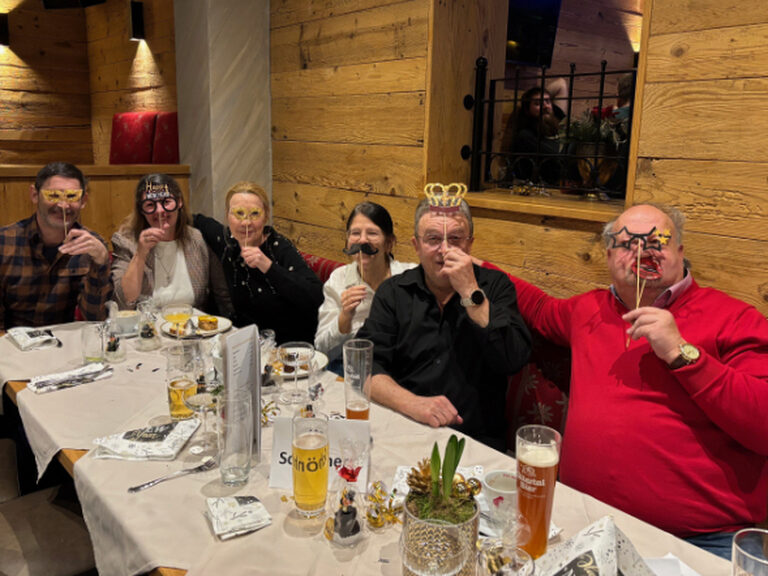 Mehrere Personen sitzen am Frühstückstisch und posieren mit lustigen Pappmasken