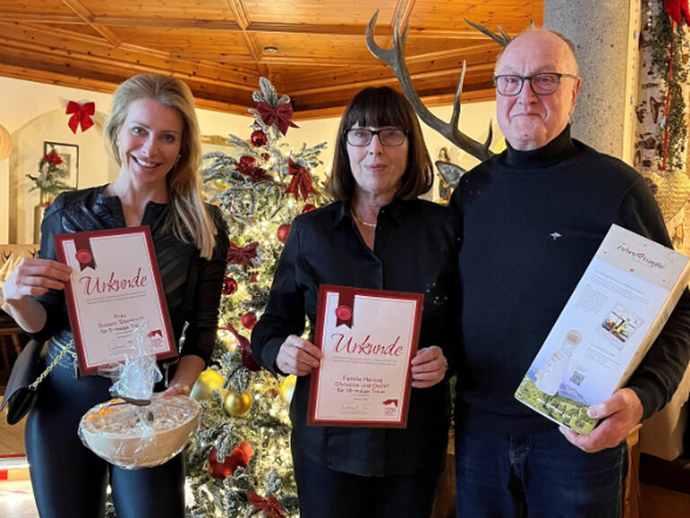 ein Paar und eine Frau posieren mit jeweils einer Urkunde und einem Geschenk vom Kohlerhof anlässlich Stammgästeehrung