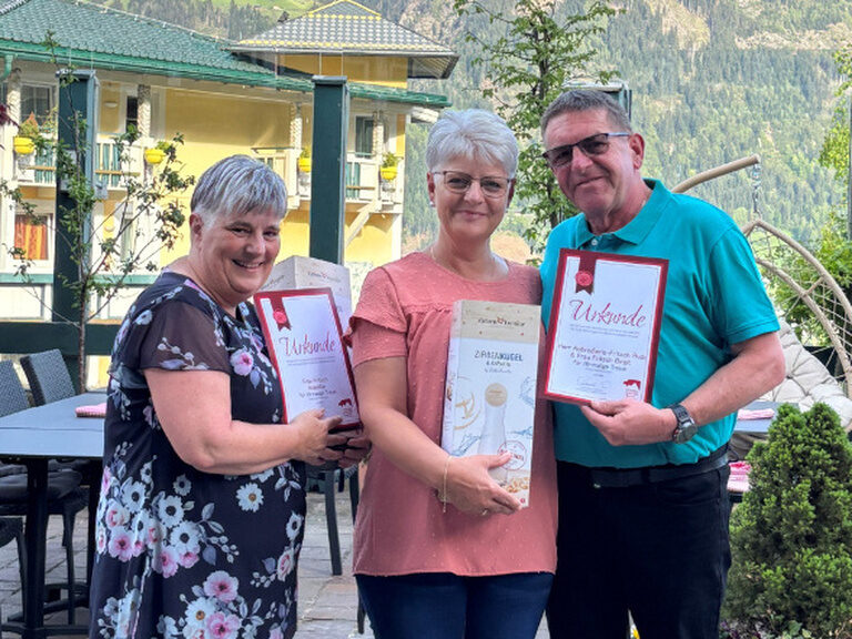 zwei Frauen und ein Mann posieren vor dem Kohlerhof mit Ehrenurkunde