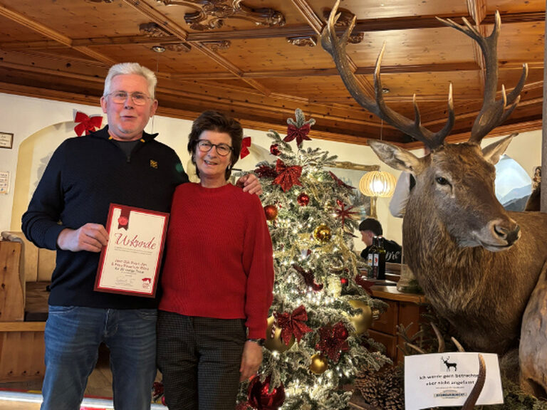Paar hält die Urkunde anlässlich Gästeehrung in der Hand, im Hintergrund ist ein beschmückter Weihnachtsbaum zu sehen