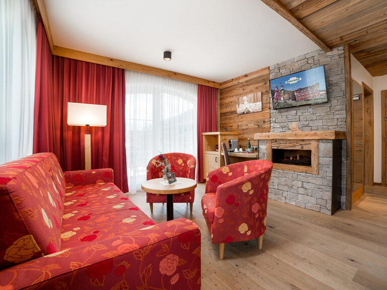 Superior Kaisersuite Das Zillertal - der Wohnbereich der Suite mit roter Couch, 2 Ohrensessel und Couchtisch