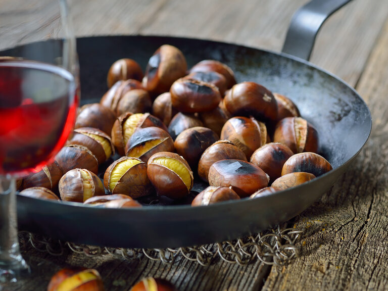 Geröstetete Esskastanien in einer schwarzen Schüssel, daneben ein Glas Rotwein