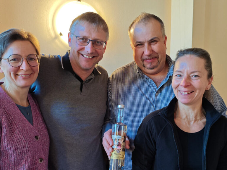 Zwei Frauen und zwei Männer lächeln in die Kamera und einer der beiden Männer hält das Geburtstagsgeschenk vom Hotel in der Hand