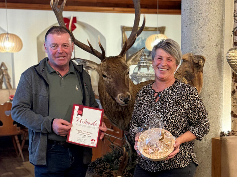 Paar posiert anlässlich Gästeehrung mit Urkunde und Geschenk