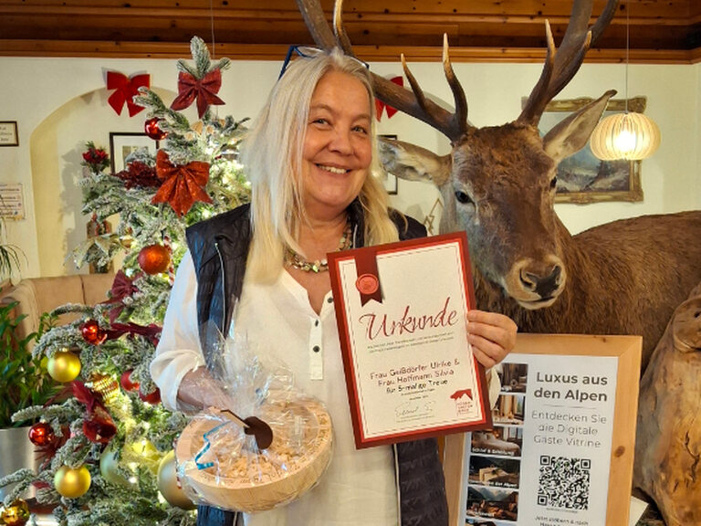 Frau lächelt in die Kamera und hält das Geschenk des Hotels sowie ihre Urkunde anlässlich ihres fünften Aufenthaltes in den Händen