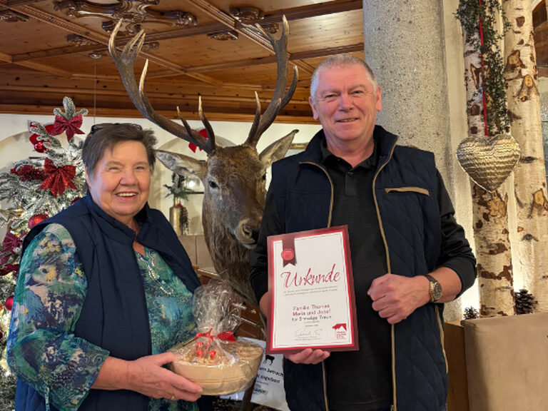 Paar posiert anlässlich Gästeehrung mit Urkunde und Geschenk